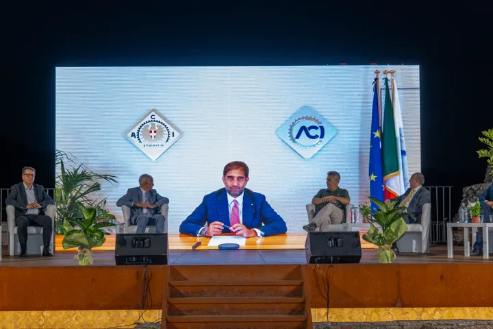 Palco con schermo e relatori nella prima fase della conferenza